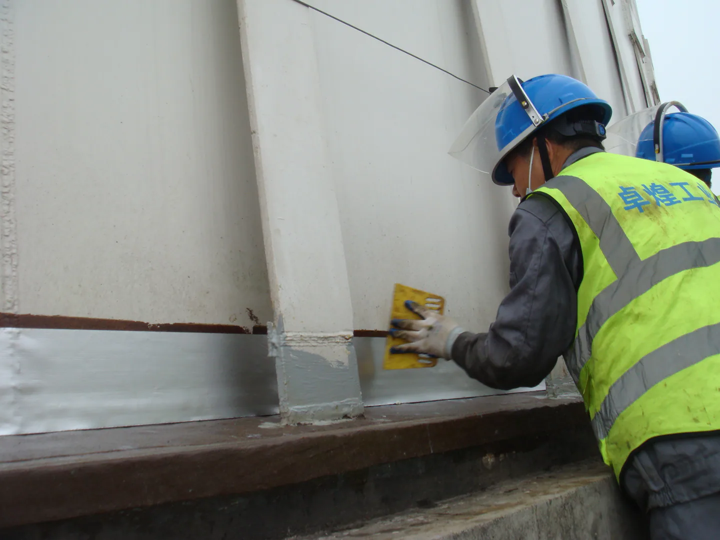 Final finishing material being applied around the protected storage tank edge.